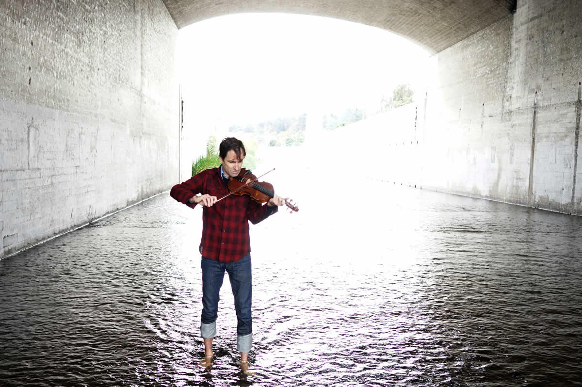 musician Andrew Bird playing violin in river